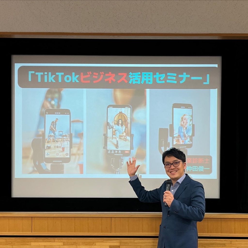 TikTokセミナーの風景写真。講師がマイクをもち、スライドの前でポーズ。　